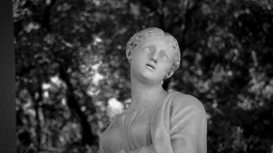 A black and white photo of a white sculpture of a forlorn woman among trees