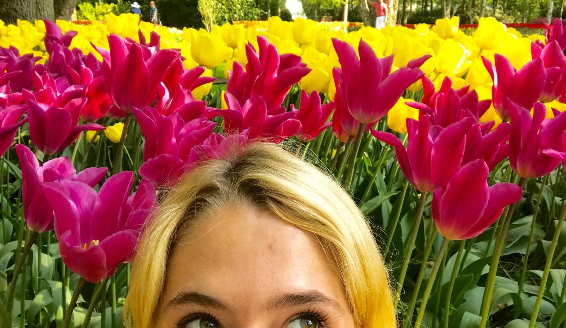 a student's face from their eyes up in front of pink and yellow tulips