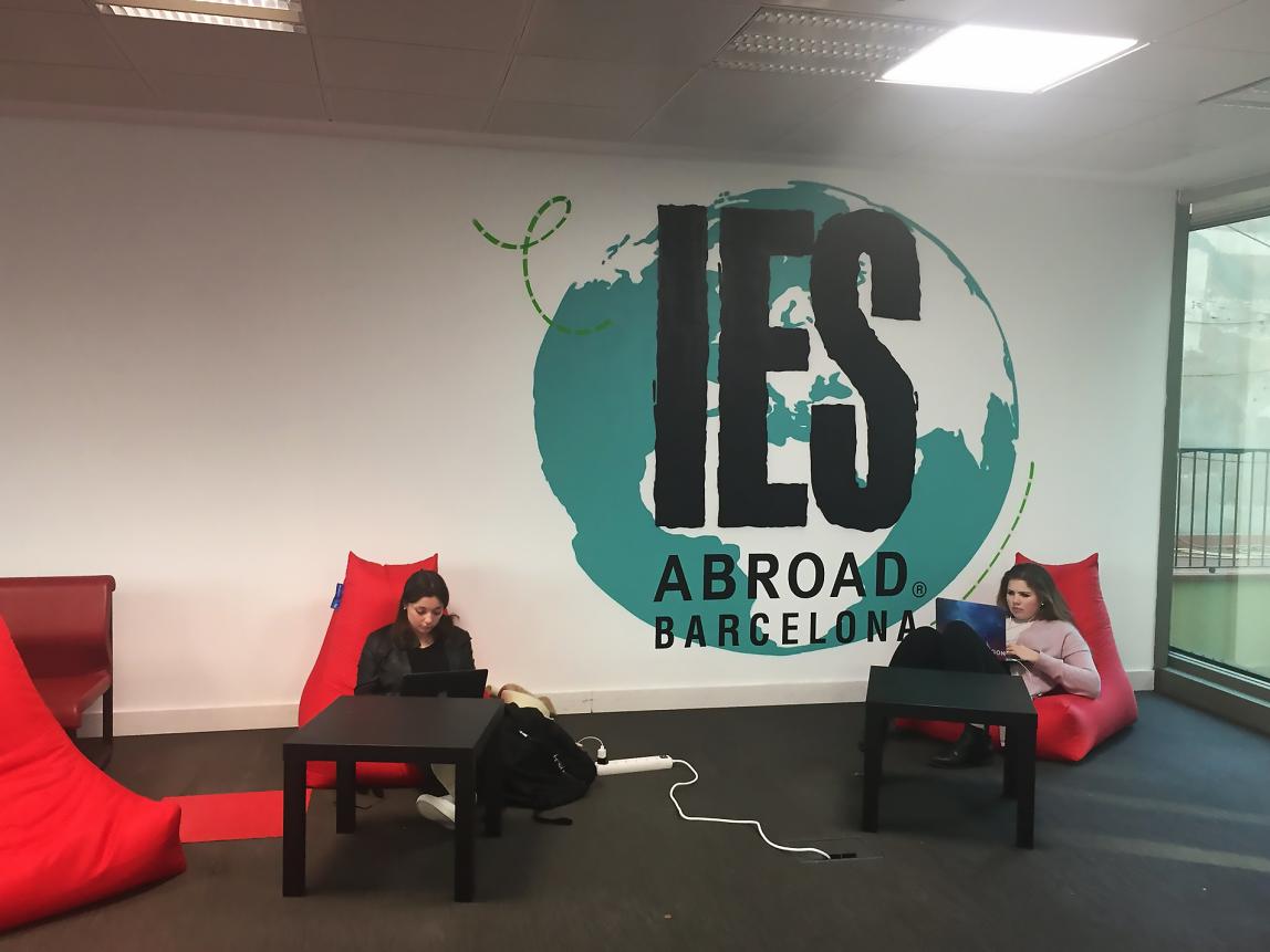 Two students sit in red lounge chairs in the Barcelona Center. Between them in a globe painted on the wall.