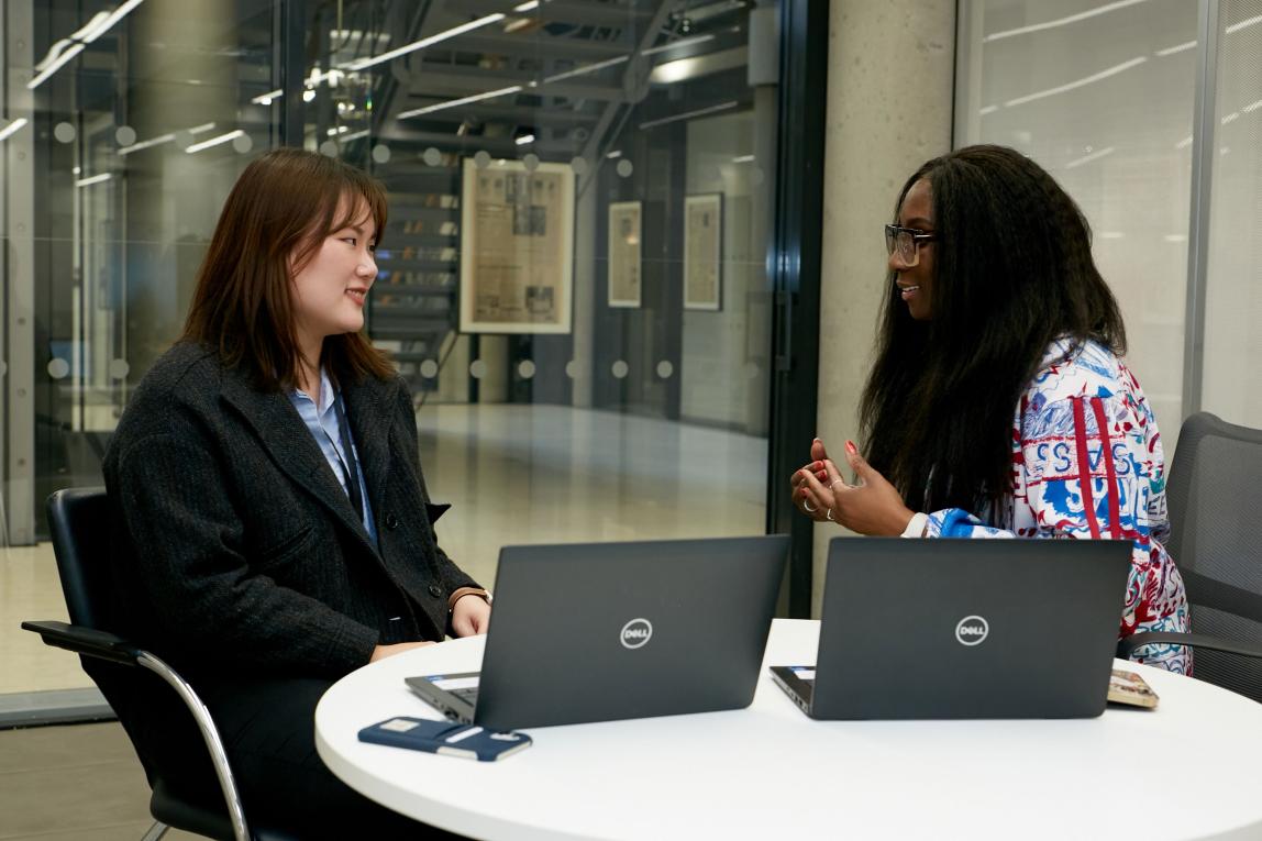 student intern sitting at desk with manager and two open laptops