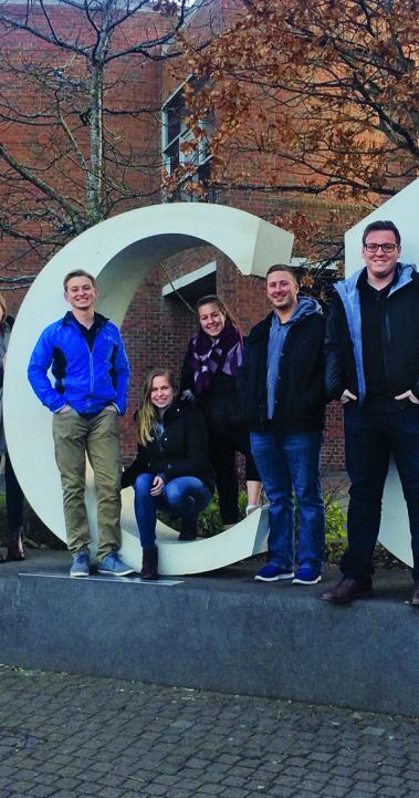 Students stand on Dublin City University's giant letter display. The letters are "DCU."