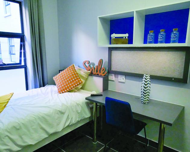 A clean bedroom featuring a twin-sized bed, a desk, and shelving with bright blue backings.