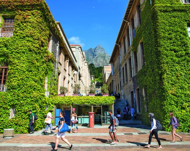 Students walk past buildings covered in lush vegetation on a sunny day at the University of Cape Town.