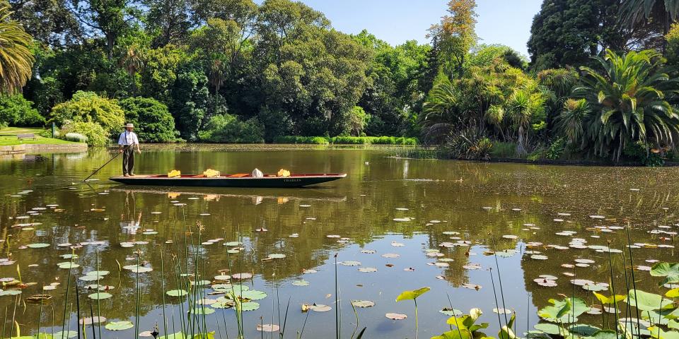 a man stands on a punting boat in the middle of a wide lake in Australia