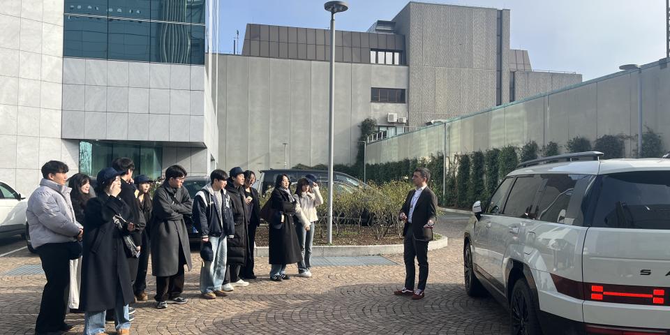 A group of SAF students standing outside listen to a presentation by a Hyundai representative